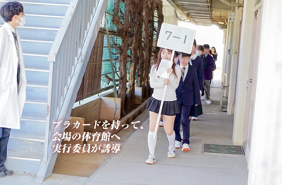 プラカードを持って、会場の体育館へ実行委員が誘導